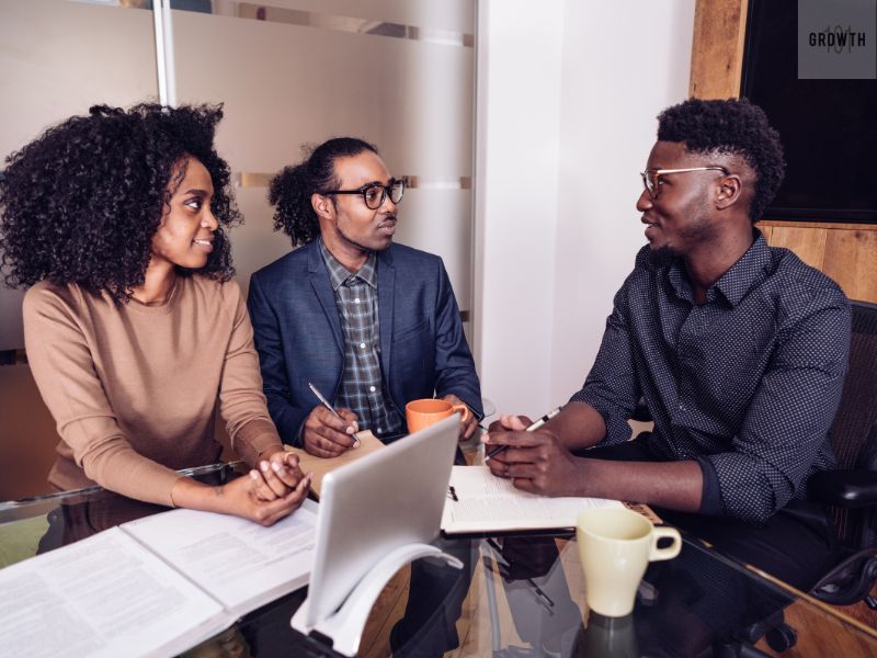 Three business professionals sitting at a table, discussing strategies and reviewing documents, symbolizing the process of securing funding for a business.