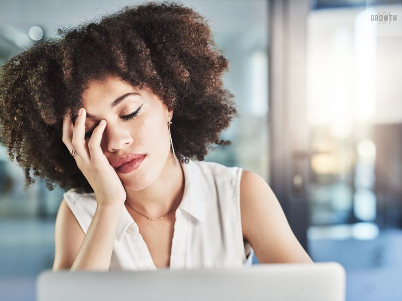 Frustrated woman sitting at her desk with hand on face, feeling overwhelmed while working on a laptop.