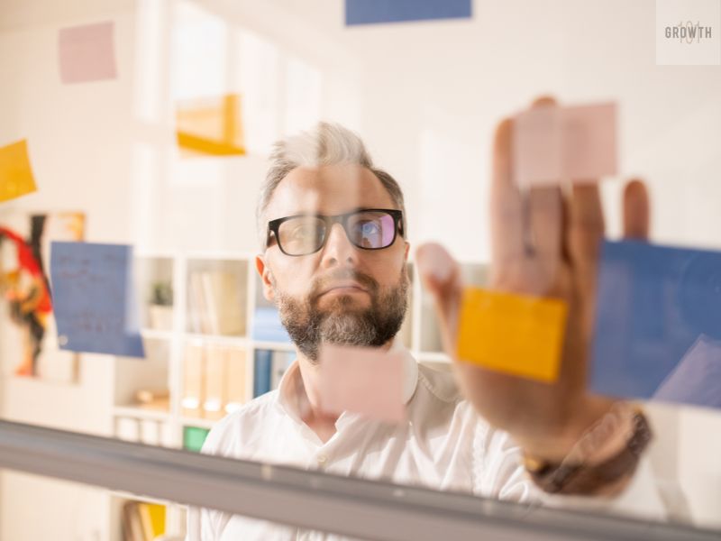 Man organizing colorful sticky notes on a glass board, representing brainstorming and finding clarity in how to find my niche.