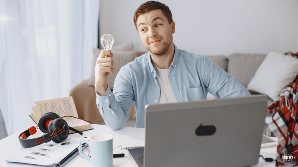 Image a on man in front of his laptop holding a lightblub representing him breaking free of the learning trap