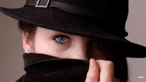 Woman's with a hat and mask with only eyes visibile. This is representing her identity