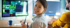 Woman smiling in front of computer screens, representing scaling your small business with project management tools and software.