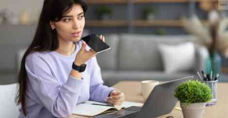 Young woman using voice search on smartphone while working on a laptop